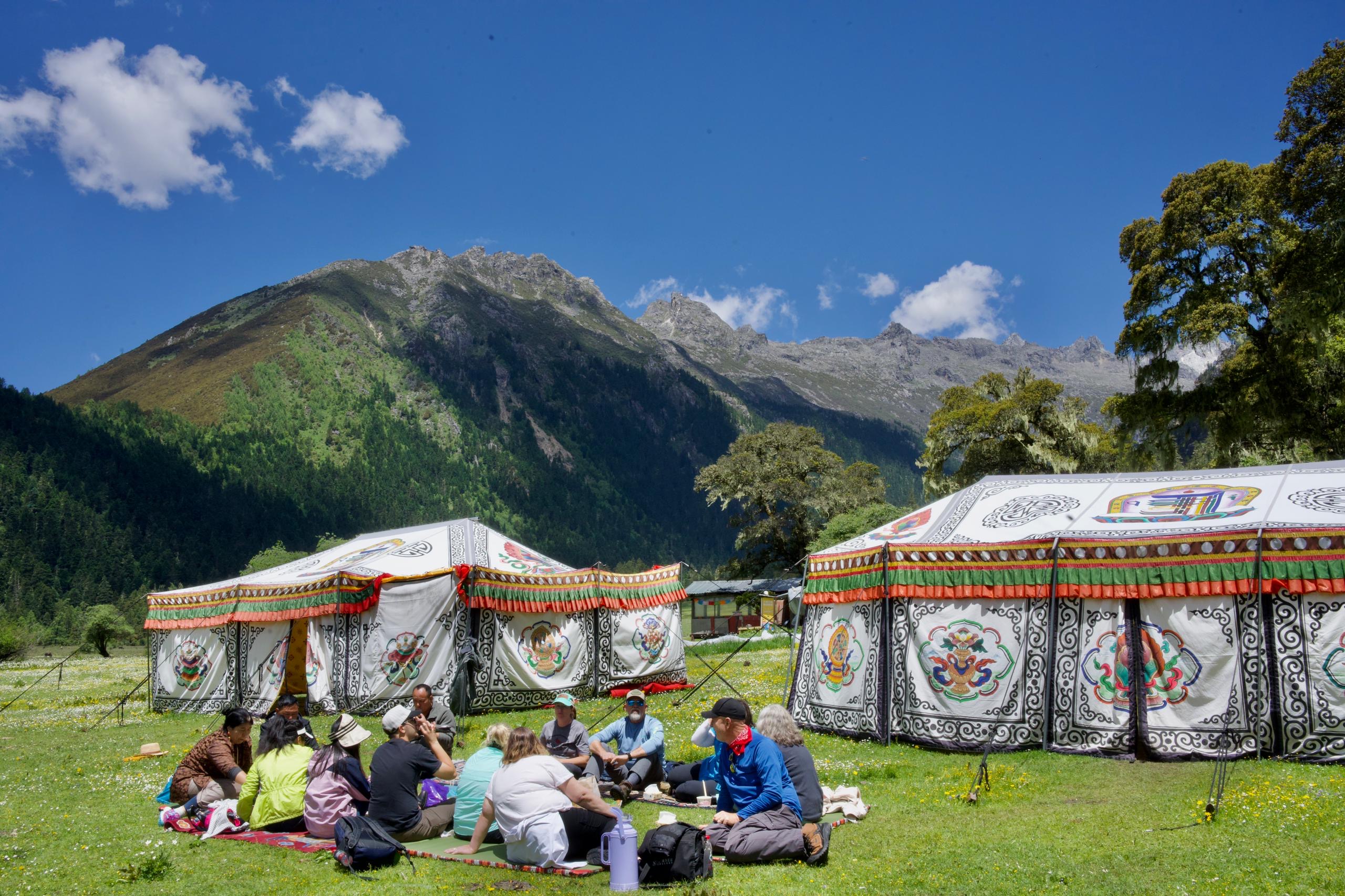 group picnic on grass in front of tents and mountains